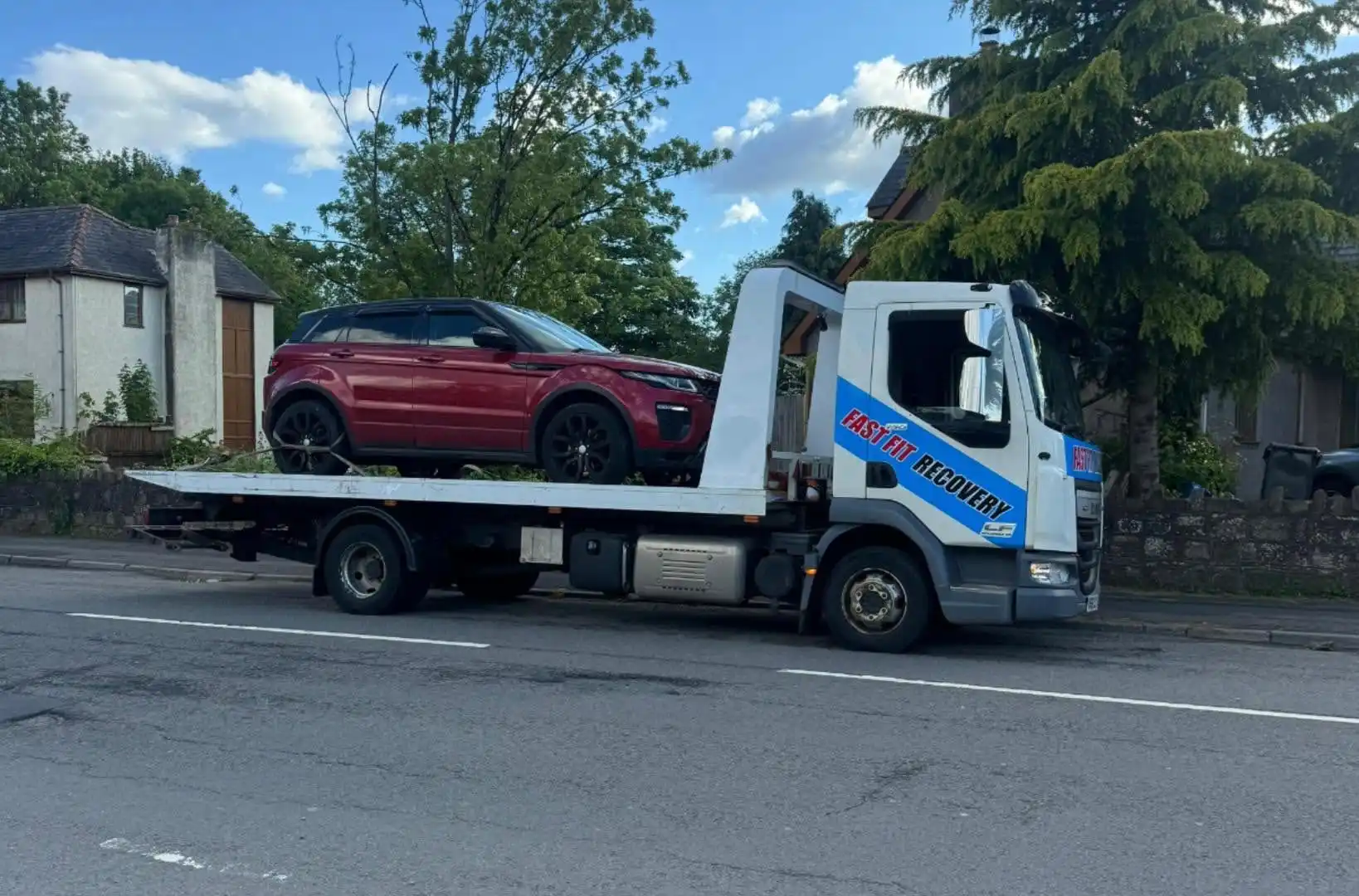 Fast Fit Recovery flatbed truck carrying a red SUV on its bed, parked on a residential road