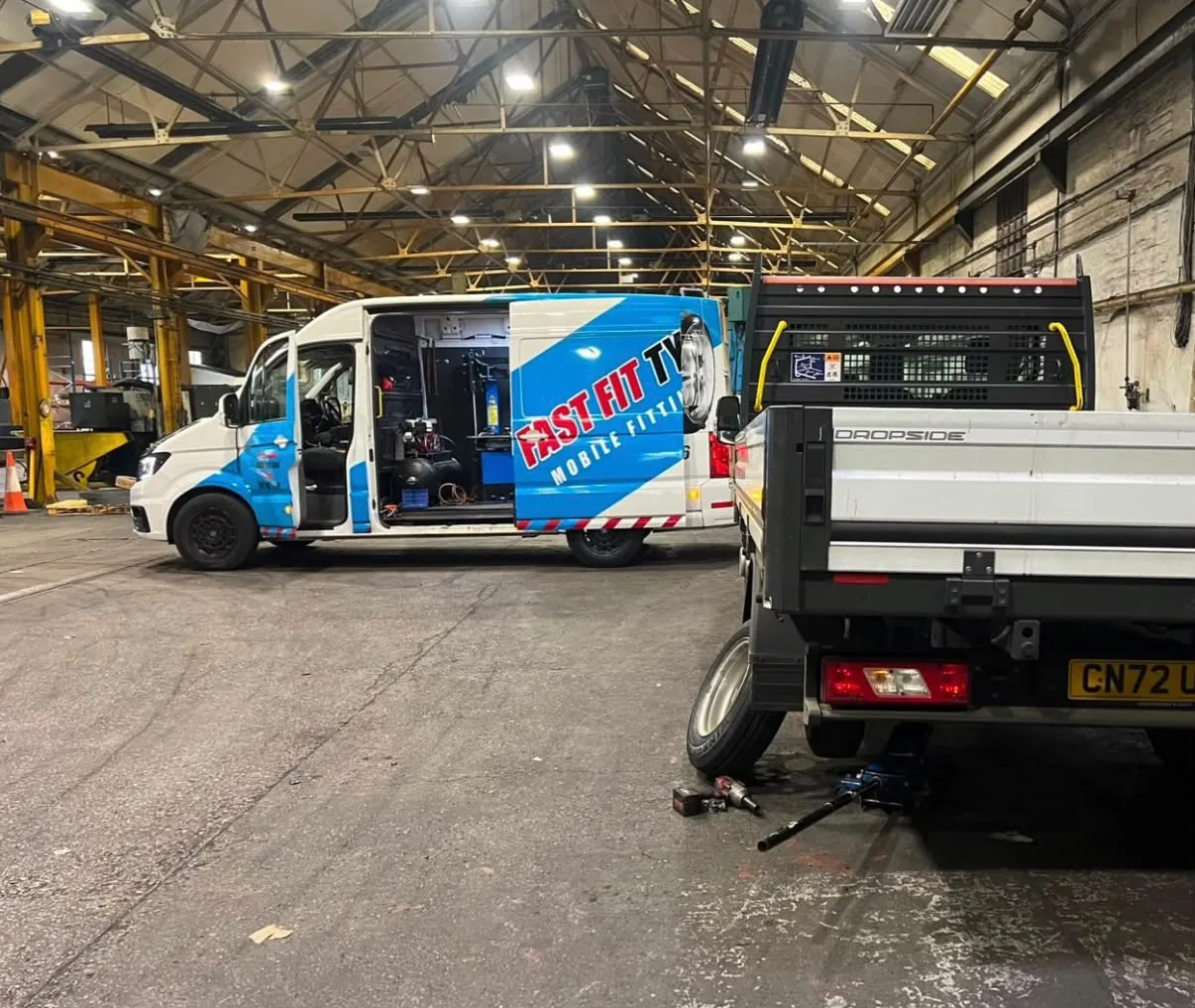 Fast Fit mobile tyre fitting van with its side door open beside a dropside truck with a rear wheel off